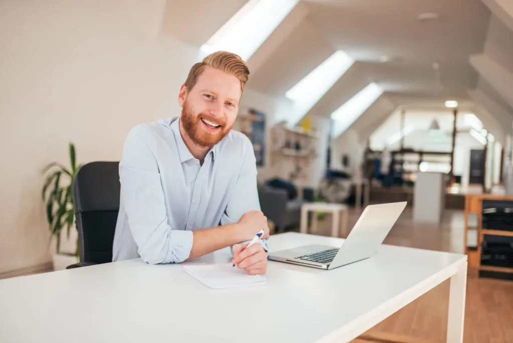 Dirigeant souriant à son bureau, ordinateur portable ouvert